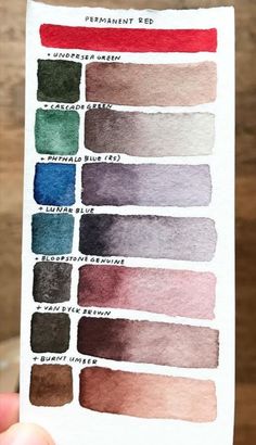 a hand holding up a watercolor swatch with different colors on the top and bottom