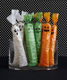 halloween candy wrapped in white and orange paper with ghost faces on them, sitting in a glass container