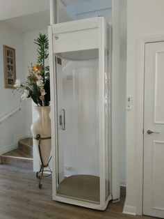 a bathroom with a white shower and wooden floor next to a vase filled with flowers