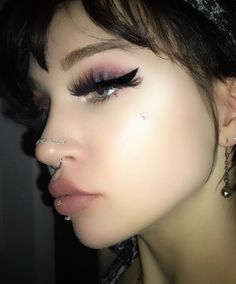 a close up of a person with fake eyelashes and piercings on their nose,