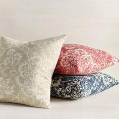 three pillows stacked on top of each other in different colors and patterns, one is red, the other blue