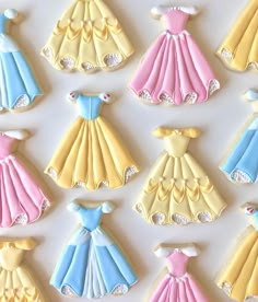 decorated cookies in the shape of princess gowns are displayed on a white tablecloth