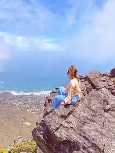 a woman sitting on top of a large rock next to the ocean