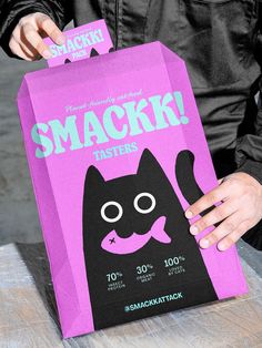 a person holding a pink bag with a black cat on it that says snack tasters