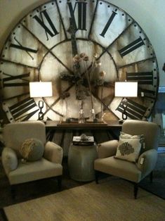 a large clock mounted to the side of a wall next to two chairs and a table