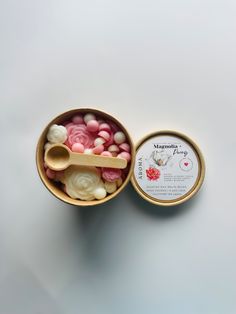 a container filled with lots of pink and white candies next to a small wooden spoon