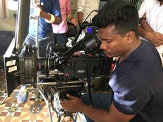 a man sitting in front of a camera on top of a tripod next to other people