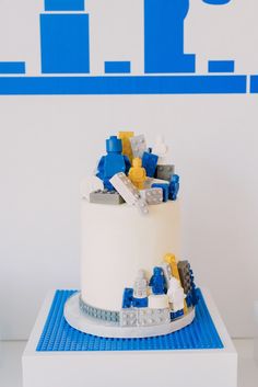 a white cake with blue and yellow legos on it sitting on a small table