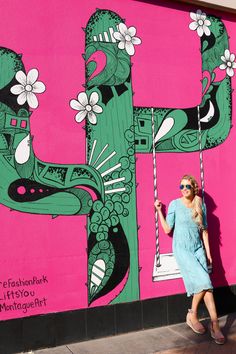 a woman standing in front of a pink wall with a mural on it's side