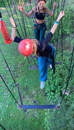 two women are zipping through the air on ropes in an outdoor area with green grass and trees