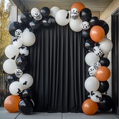 an arch made out of black, white and orange balloons is decorated with skulls and pumpkins