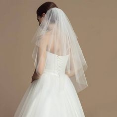 the back of a bride's wedding dress with a veil on her head and shoulder