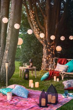 an outdoor area with lights, pillows and blankets on the ground next to some trees