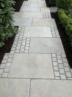 a walkway made out of pavers stone surrounded by shrubbery