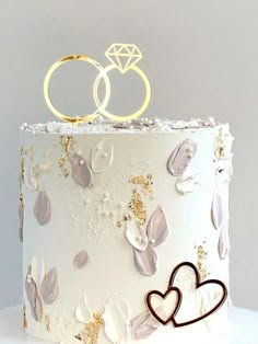 two wedding rings on top of a white cake with gold leaf decorations and pink flowers