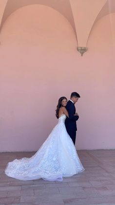 a bride and groom standing in front of a pink wall