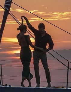 two people standing on top of a boat at sunset