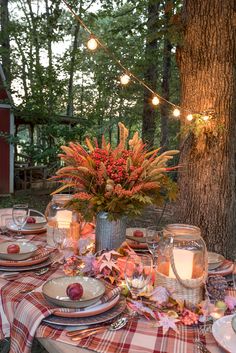 a table set with plates, candles and flowers in front of a tree at night