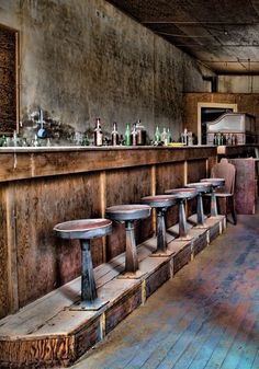 an old bar with stools and bottles on the wall