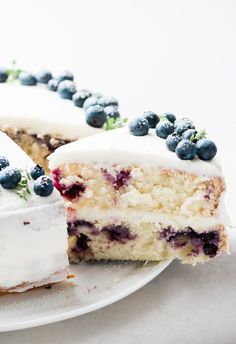 a white cake with blueberries and frosting on a plate next to a slice cut from it