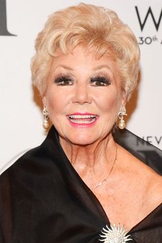 an older woman with blonde hair wearing a black dress and diamond brooch on her left shoulder