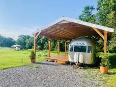 an rv is parked under a covered area in the middle of a field with benches