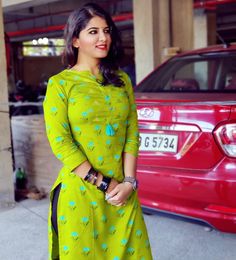 a woman standing in front of a red car wearing a green dress with blue flowers on it