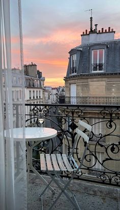 a balcony with two chairs and a table on it, overlooking the city at sunset