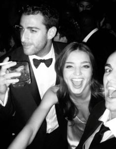 two men and a woman are posing for a photo at an event with drinks in their hands