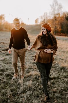 a man and woman walking through a field holding hands