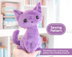 a purple cat stuffed animal sitting on top of a person's hand in front of bookshelves