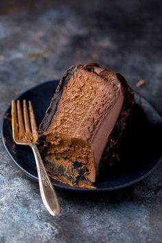 a piece of chocolate cake on a black plate with a fork and knife next to it