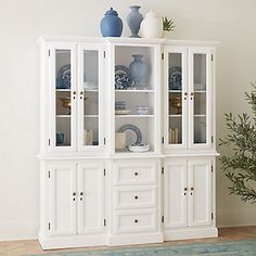 a white china cabinet with blue vases on top