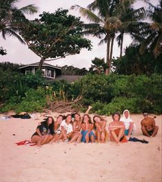 a group of young people sitting on top of a sandy beach next to palm trees