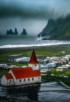 a small white church with a red roof near the ocean