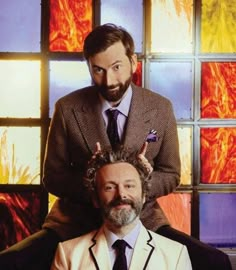 a man with a beard sitting next to another man in front of stained glass windows