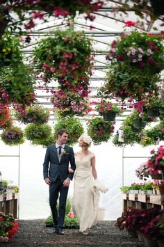 a bride and groom walking through a greenhouse filled with hanging flower baskets for their wedding ceremony