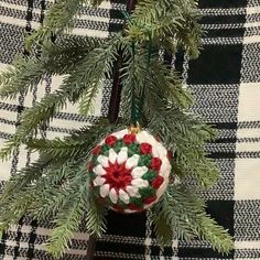 a christmas ornament hanging from a tree branch with red and white flowers on it