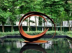 a sculpture in the middle of a pond surrounded by trees