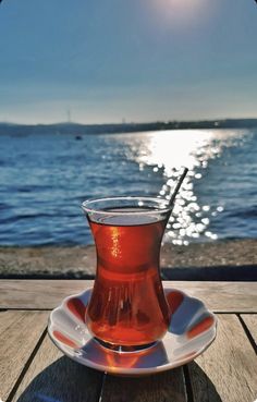 a tea cup sitting on top of a wooden table next to the ocean with a straw in it