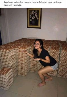 a woman kneeling on the floor in front of stacks of bread boxes and pointing at something