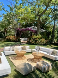 an outdoor living area with couches, tables and pillows on the grass in front of some trees