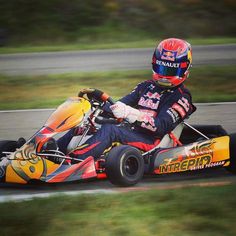 a man riding on the back of a yellow and red kart racing car down a race track