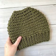 a hand is holding up a green knitted beanie on a white wooden floor