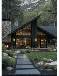 a house that is surrounded by rocks and grass with lights on the windows, along with stone steps leading up to it