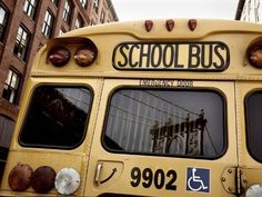 a yellow school bus parked in front of a tall building on a street with buildings behind it