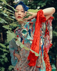 a woman with blue hair and red scarf on her neck standing in front of trees