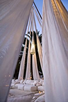 an outdoor area with white curtains and pillows on the ground, lit up by candles