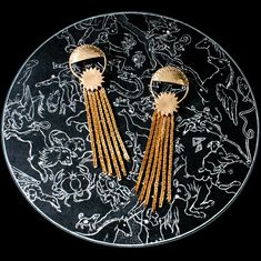 a pair of gold - tone earrings on a black and white plate with intricate designs