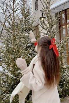 a woman in white coat standing next to snow covered trees and holding a stuffed animal